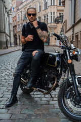 Portrait of attractive man biker with tattooes posing on his motorcyle in alleyway downtown.