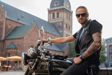 Shot of tattooed urban biker dressed in stylish clothes driving motorcycle in city.