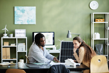 Two colleagues sitting at table at office and examining alternative energy project together