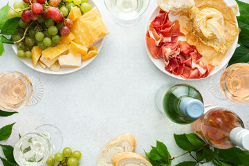 Top view of table with rose and white wine in glasses, plates with grapes, cheese and jamon, baked...