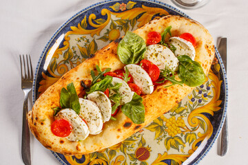 Base di pizza napoletana con sopra mozzarella di bufala, pomodori rossi, basilico fresco e origano