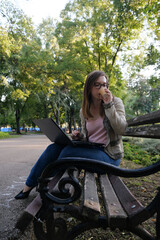 Obraz na płótnie Canvas Young woman drinking coffee and working on a laptop in the park