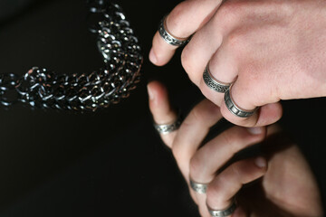 Young man's hand with metal rings on fingers takes a jewelry chain from the mirror, fashion and...