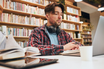 Students learning in university library. Young man preparing for test on laptop. Girl learning from book. Focused students studying for college exams Students discussing and learning together