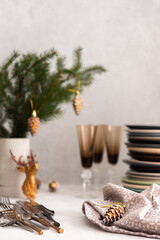Preparing for a festive table setting, a stack of different plates and forks with knives, fir branches in a concrete vase, Christmas decorations