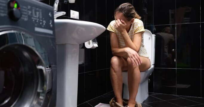 Young woman is crying in pain while sitting on toilet