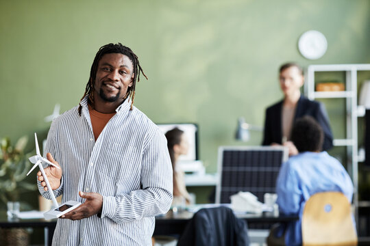 Portrait of African engineer with windmill model smiling at camera while standing at office