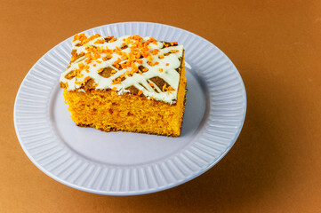 slice of carrot cake with white cream on a brown background