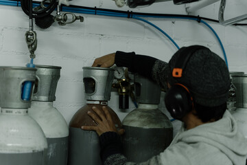 Man in cap and helmet in a room checking oxygen tanks for diving
