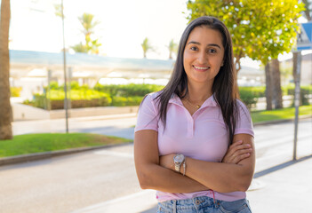 Young beautiful hispanic brunette woman wearing polo shirt standing with arms folded in the city....