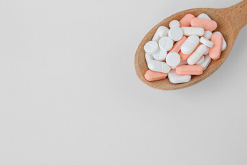 Many different pills in wooden spoon on white background. Copy space. Top view