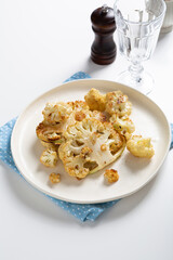 Vegetarian roasted cauliflower steak on white plate close up food