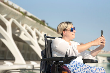 Fototapeta na wymiar portrait of a smiling woman with disability in a wheelchair with sunglasses taking a selfie picture