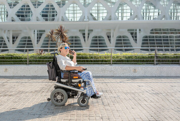 Tourist talking on smartphone in electric wheelchair on a city street