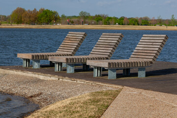 Three oversized outdoor wooden chaise lounges chairs on the waters edge of a lake.