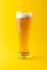 Gordijnen Vertical image of full pint glass of lager beer on yellow background, with copy space © vectorfusionart