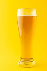 Gordijnen Vertical image of nearly full pint glass of lager beer on yellow background, with copy space © vectorfusionart