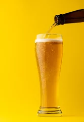 Gordijnen Image of beer bottle pouring into pint glass of lager beer, with copy space on yellow background © vectorfusionart