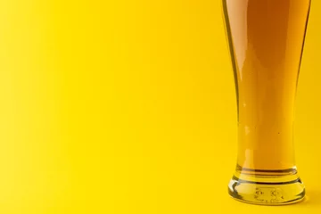 Gordijnen Horizontal image of pint glass of lager beer on yellow background, with copy space © vectorfusionart