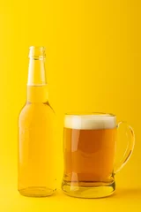 Gordijnen Image of full clear glass bottle and glass tankard of lager beer, with copy space on yellow © vectorfusionart