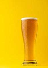 Image of full pint glass of lager beer, with copy space on yellow background