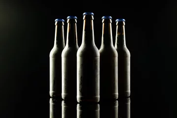 Gordijnen Horizontal image of five dark glass bottles of lager beer with blue crown caps on black background © vectorfusionart