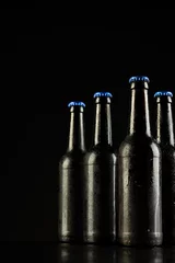 Gordijnen Vertical image of four dark glass bottles of lager beer with blue caps on black, with copy space © vectorfusionart