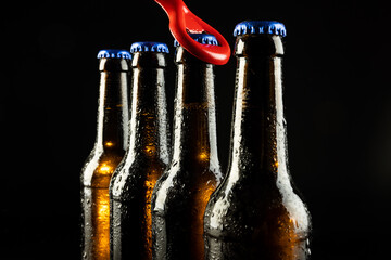 Image of red bottle opener and four beer bottles with blue crown caps, with copy space on black - obrazy, fototapety, plakaty
