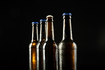 Image of four beer bottles one open the rest with blue crown caps, with copy space on black - obrazy, fototapety, plakaty