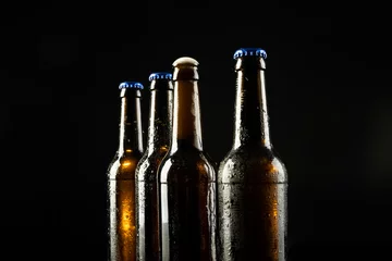 Foto op Canvas Image of four beer bottles one open the rest with blue crown caps, with copy space on black © vectorfusionart