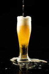 Vertical image of lager beer dripping into overflowing pint glass on black, with copy space
