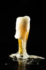 Schilderijen op glas Image of overflowing pint glass of foamy beer, with copy space on black background © vectorfusionart