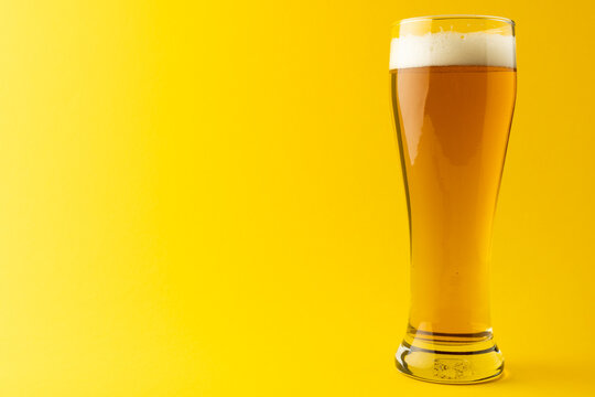 Image of full pint glass of lager beer, with copy space on yellow background
