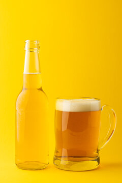 Image of full clear glass bottle and glass tankard of lager beer, with copy space on yellow