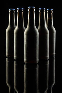 Vertical image of five dark glass bottles of lager beer with blue caps on black, with copy space
