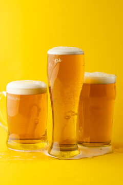 Image of three different full pint glasses of lager beer, with copy space on yellow background