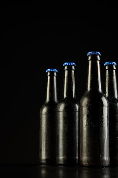 Vertical image of four dark glass bottles of lager beer with blue caps on black, with copy space
