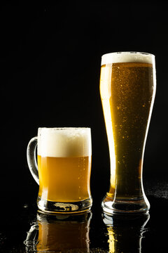 Vertical image of pint glass and glass tankard of lager beer on black background, with copy space