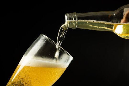 Horizontal image of clear bottle of lager beer pouring into glass on black, with copy space