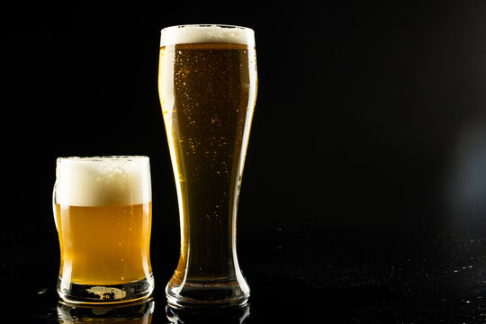 Image of full pint glass and tankard of foamy beer, with copy space on black background