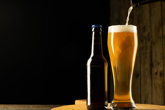 Image of full beer bottle and beer pouring into pint glass, with copy space