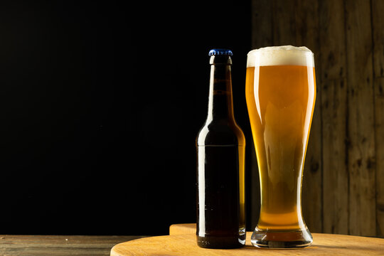 Image of full bottle and pint glass of beer on wooden table, with copy space