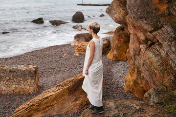thoughtful hipster woman wearing dress near sea in autumn