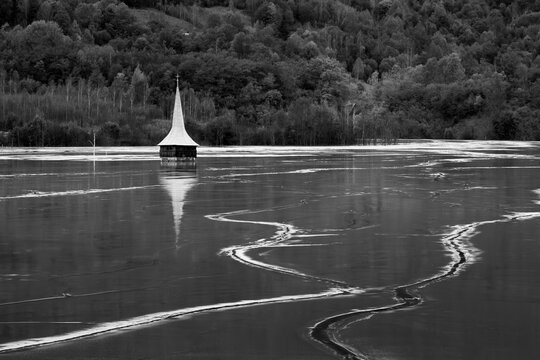 Grayscale shot of a Lonely church uin the water with forest rees in the backgroundr