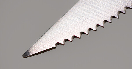 Close-up of the tip of a bread knife on gray background.