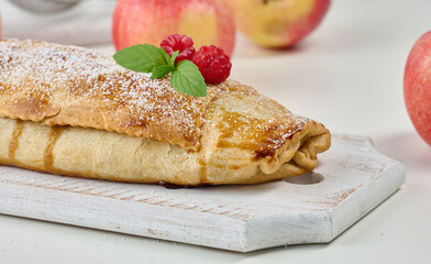 Baked strudel with apples sprinkled with powdered sugar on a white wooden board, delicious dessert