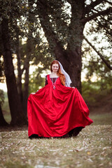 Portrait of a red-haired woman in a historical costume of the 15th century - a red silk dress in the fashion of Venice.  Lady running through the forest