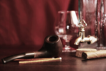 Moody man's table in cabinet with cognac, smoking pipe, matches, bottle. Leisure activity and evening relax concept