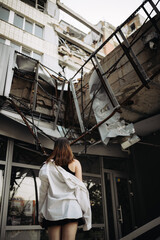 a girl stands near a destroyed house