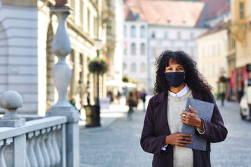 businesswoman standing in street with face mask holding folder with documents